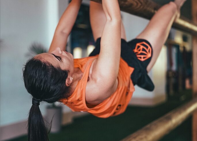 A woman in athletic clothes climbing and hanging upside down